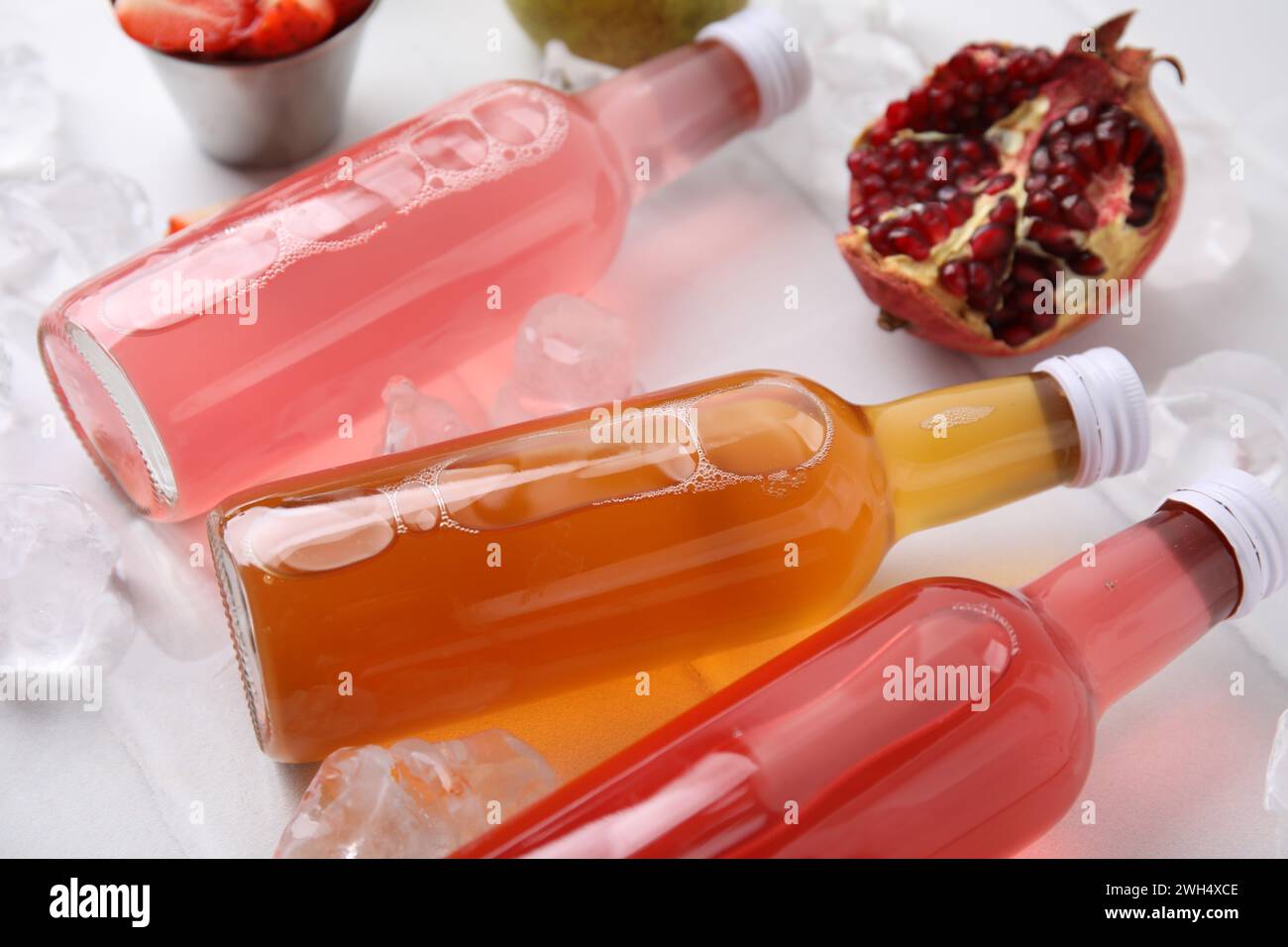 Savoureux kombucha dans des bouteilles en verre, des fruits frais et de la glace sur la table blanche, gros plan Banque D'Images