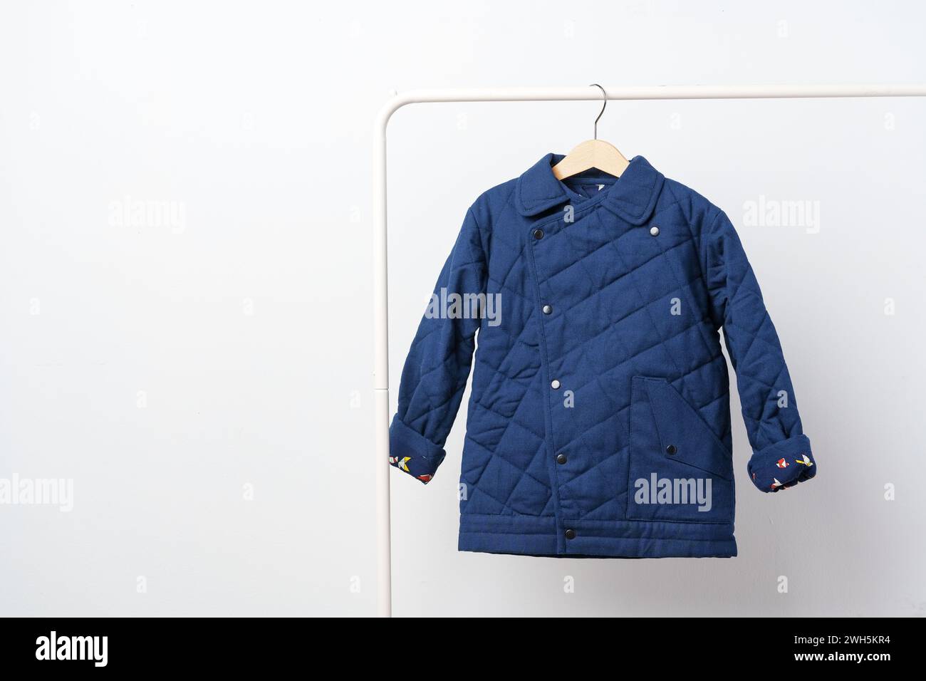 Manteau bleu matelassé pour enfants sur cintre contre mur blanc Banque D'Images