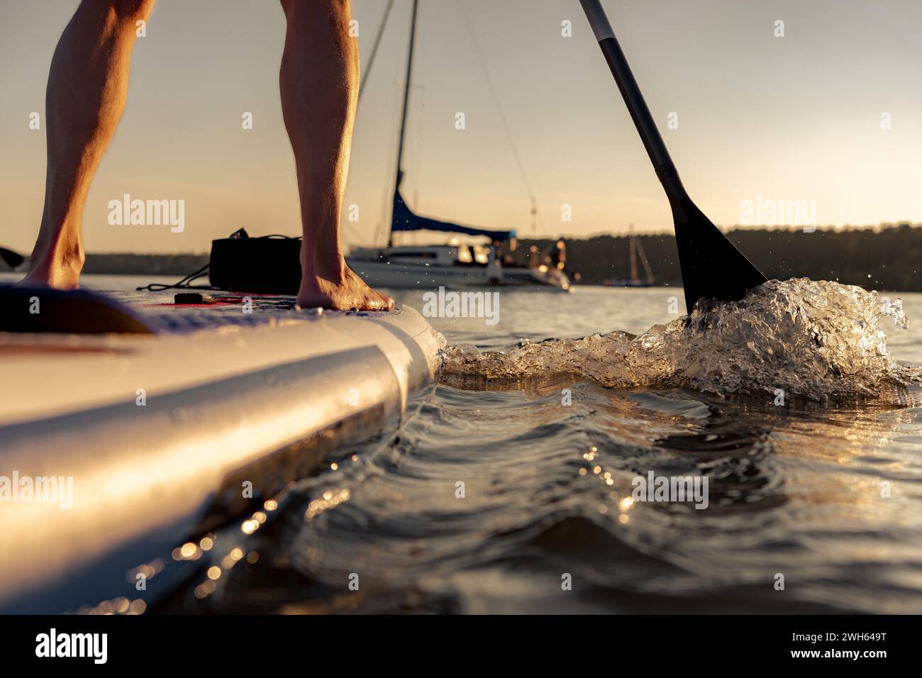 Photo rapprochée de l'homme surfeur jambes est debout sur stand up paddle sup planche au coucher du soleil calme lac Banque D'Images