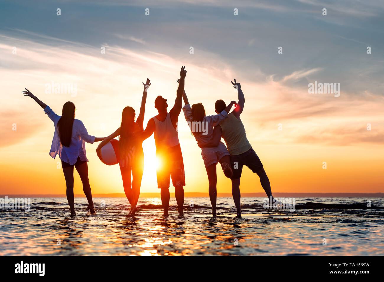 Cinq jeunes amis heureux s'amusent, debout ensemble, embrassant et rencontrant le coucher du soleil à bras ouverts sur la plage calme du lac coucher du soleil Banque D'Images