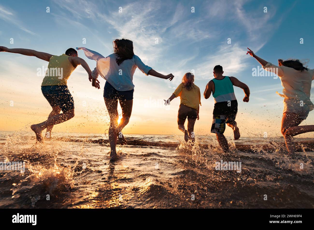 Groupe de jeunes amis heureux s'amusent, des courses et des sauts à la plage du coucher du soleil avec beaucoup d'éclaboussures Banque D'Images