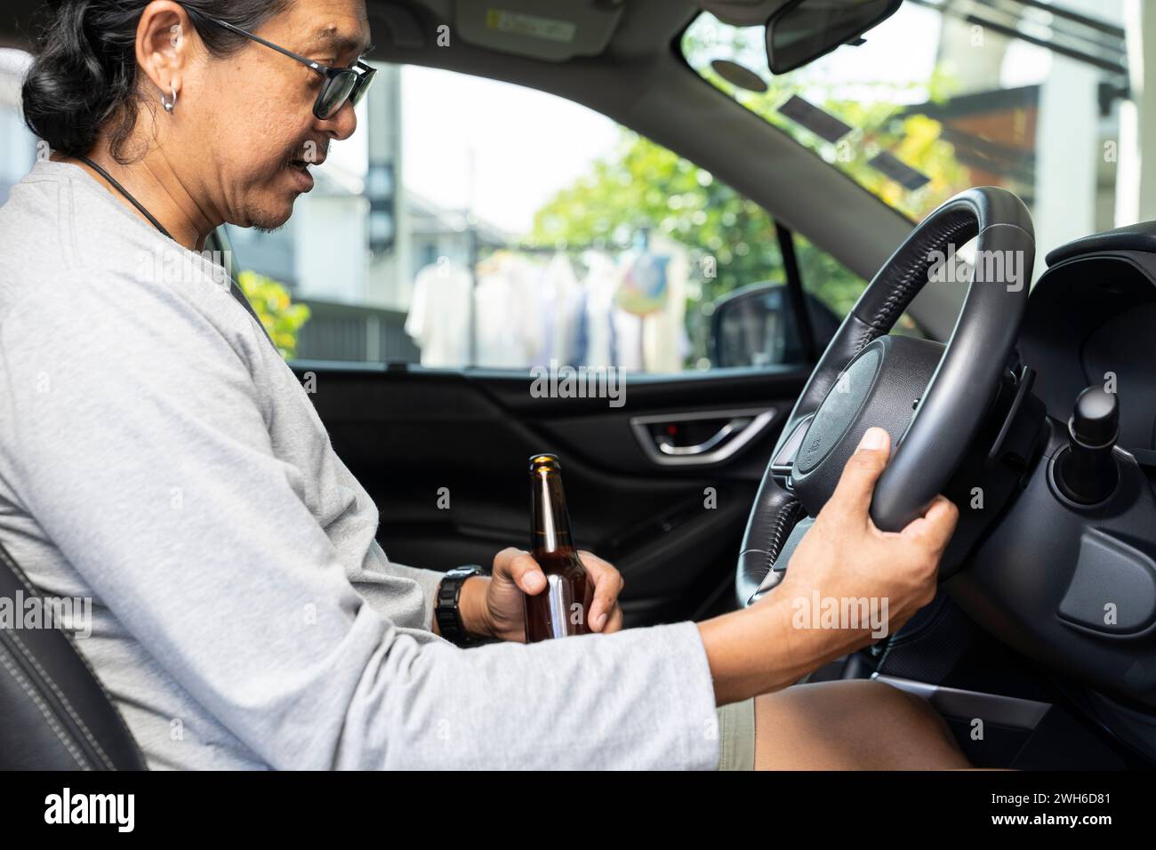 Un jeune homme asiatique ivre conduit une voiture avec une bouteille de bière, concept de conduite dangereux. Banque D'Images