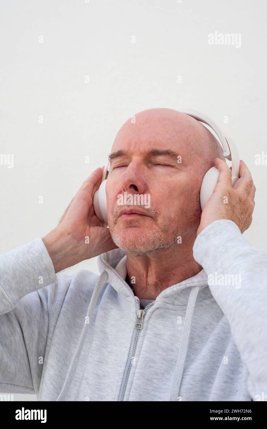 homme chauve mature portant des écouteurs écoutant de la musique avec les yeux fermés. Banque D'Images