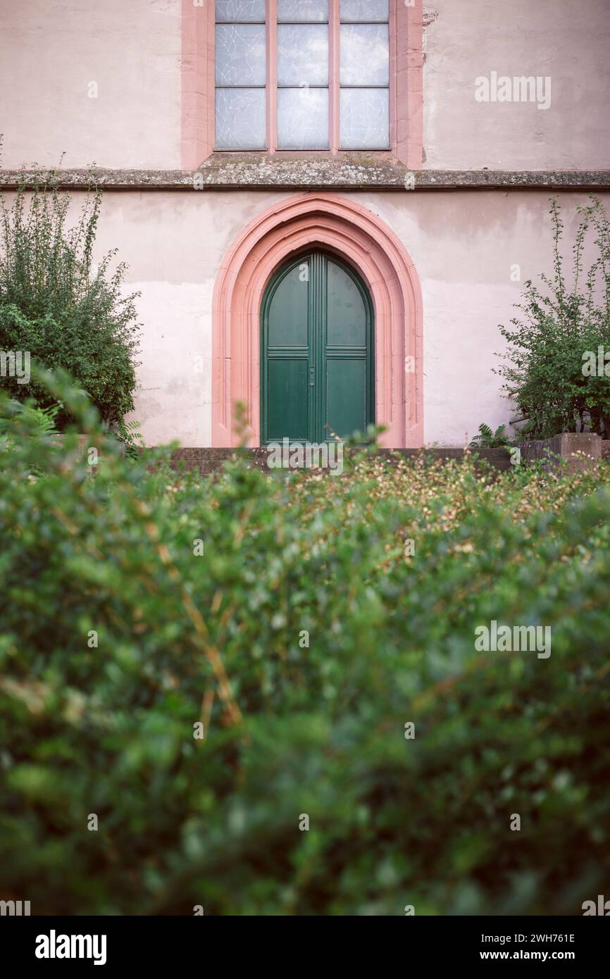 Une porte d'église voûtée gothique verte encadrée de pierre rose vue sur une haie ; église St Stephan, Mayence. Banque D'Images