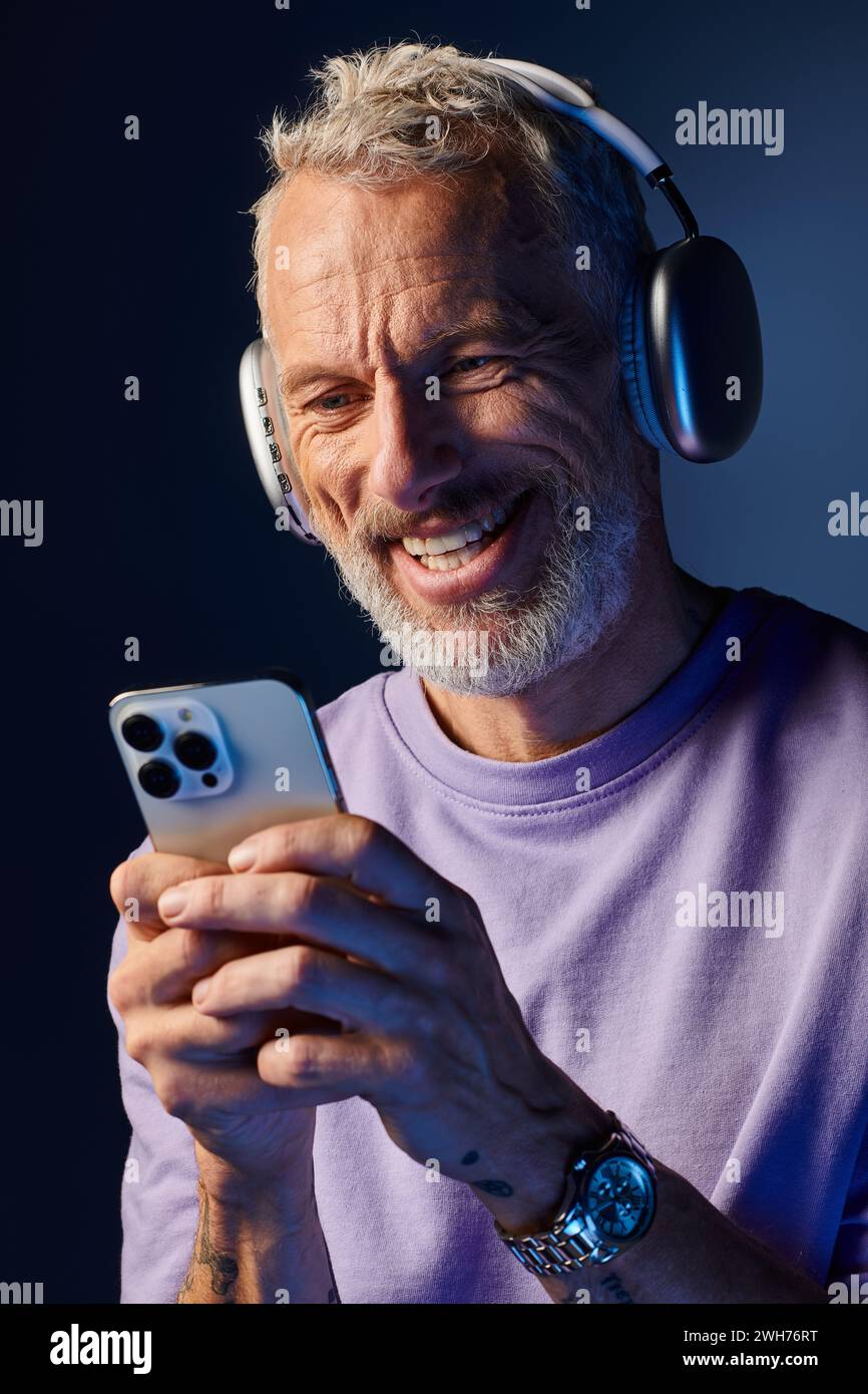 joyeux homme mûr beau avec barbe et écouteurs appréciant la musique et regardant son téléphone Banque D'Images