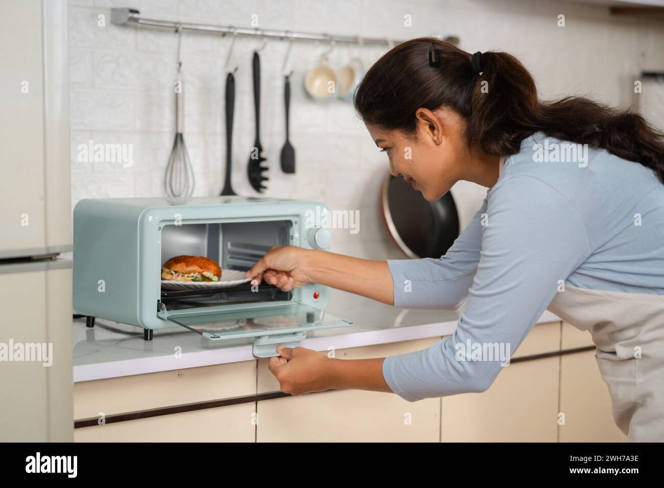 Indienne heureuse femme souriante cuisinant un hamburger en le plaçant sur un four à micro-ondes à la cuisine - concept d'une alimentation saine, d'un mode de vie domestique et de la technologie Banque D'Images