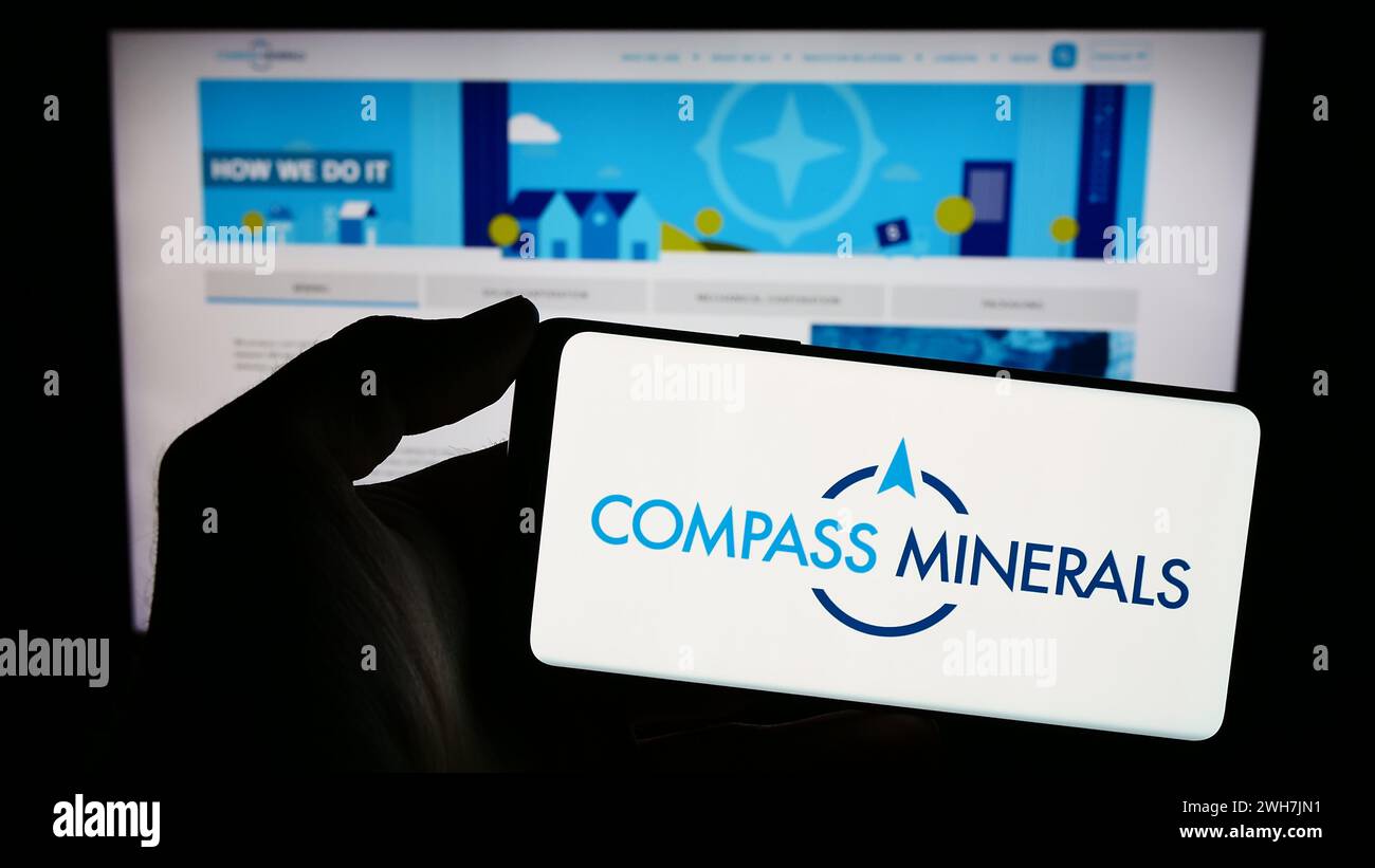 Personne tenant le téléphone portable avec le logo de la société minière américaine Compass Minerals International Inc en face de la page Web. Concentrez-vous sur l'affichage du téléphone. Banque D'Images
