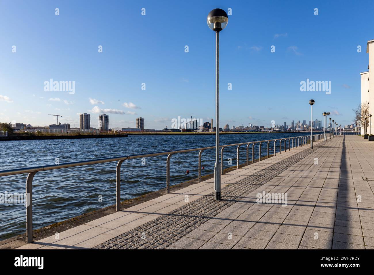 Le long de la Tamise dans l'est de Londres, une large passerelle en face de l'aéroport de London City. Beau temps ensoleillé avec un ciel bleu clair et des lampadaires. Banque D'Images