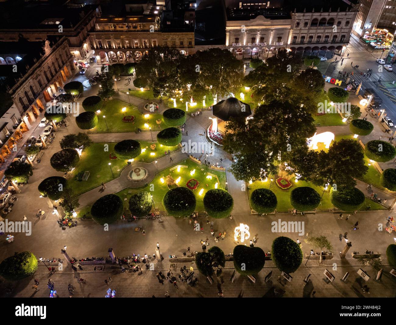 Vue aérienne nocturne de la place principale animée de Morelia avec son kiosque central et les visiteurs qui flânent, illuminés par des lumières chaudes. Banque D'Images