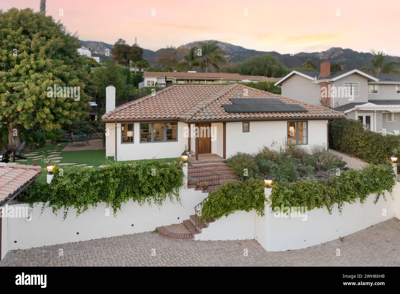 Maison avec toit en tuiles, mur de pierre et buissons luxuriants au premier plan Banque D'Images