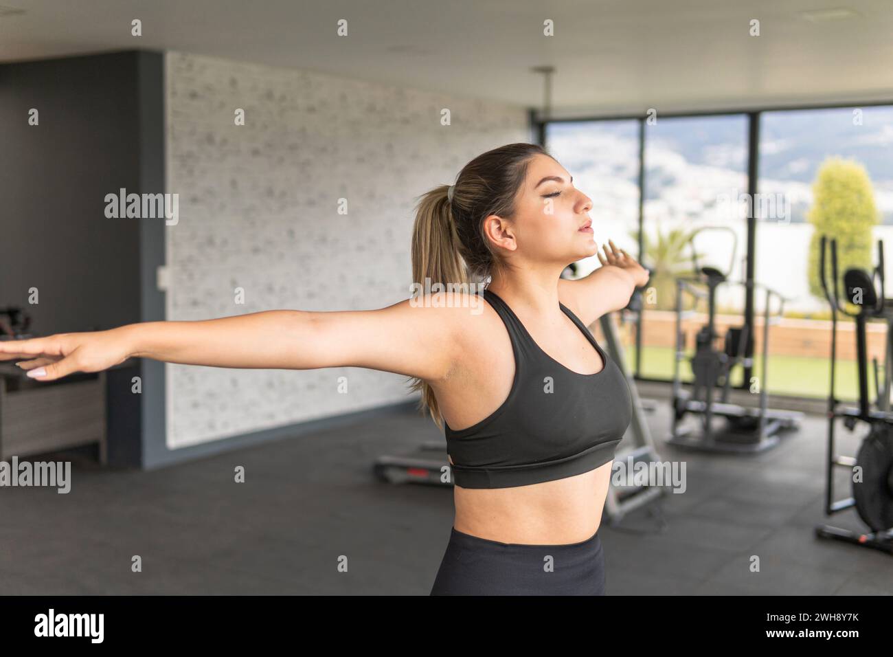 Jeune femme respirant et faisant de l'exercice dans un gymnase avec les bras ouverts Banque D'Images