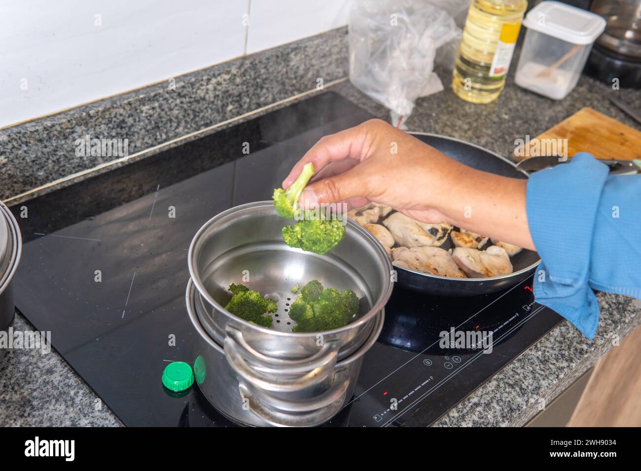 main d'homme plaçant le brocoli dans un cuiseur vapeur sur une cuisinière à induction Banque D'Images