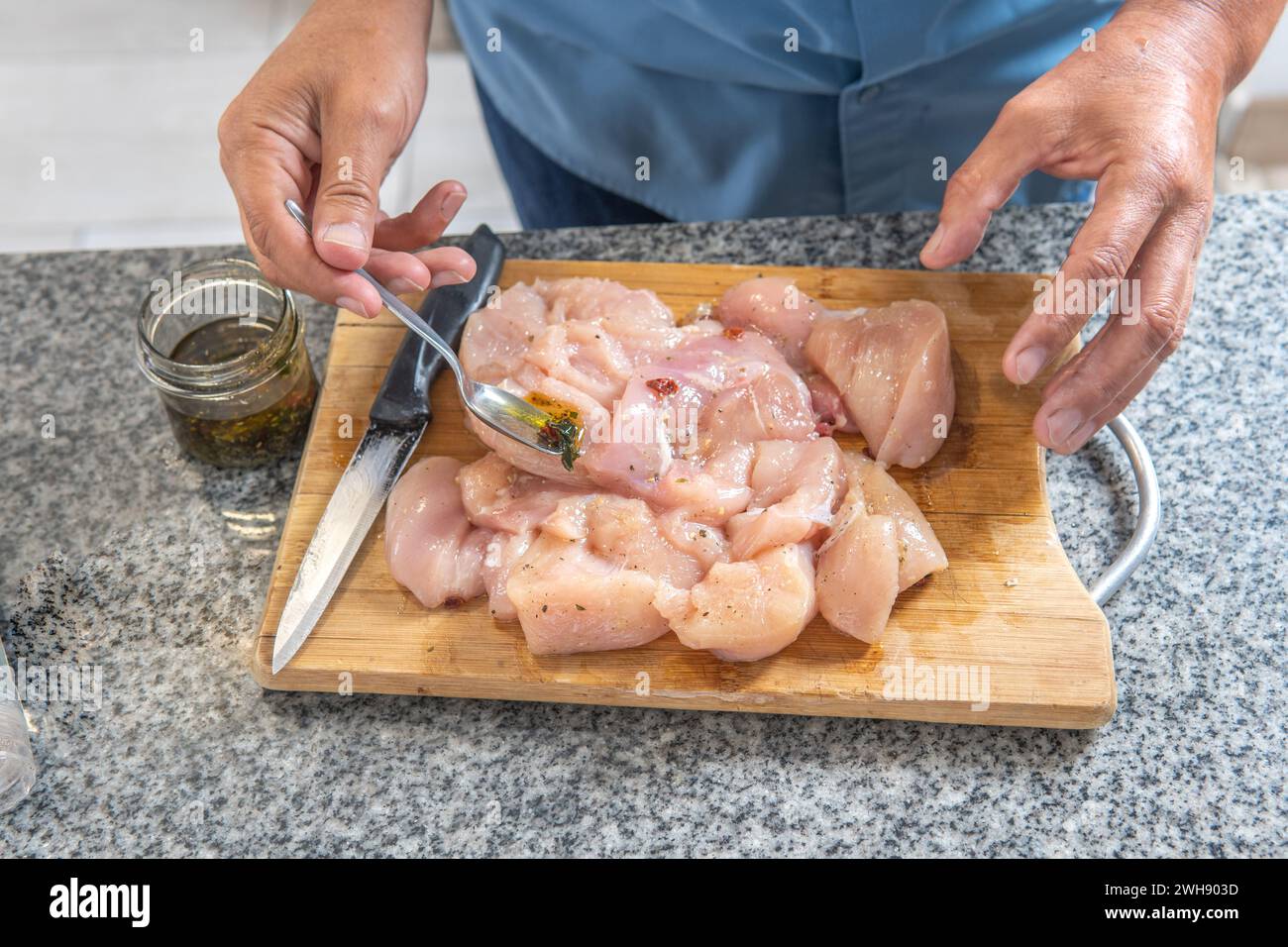 mains de l'homme mettant l'assaisonnement sur un poulet cru pour le cuire sur une planche à découper Banque D'Images