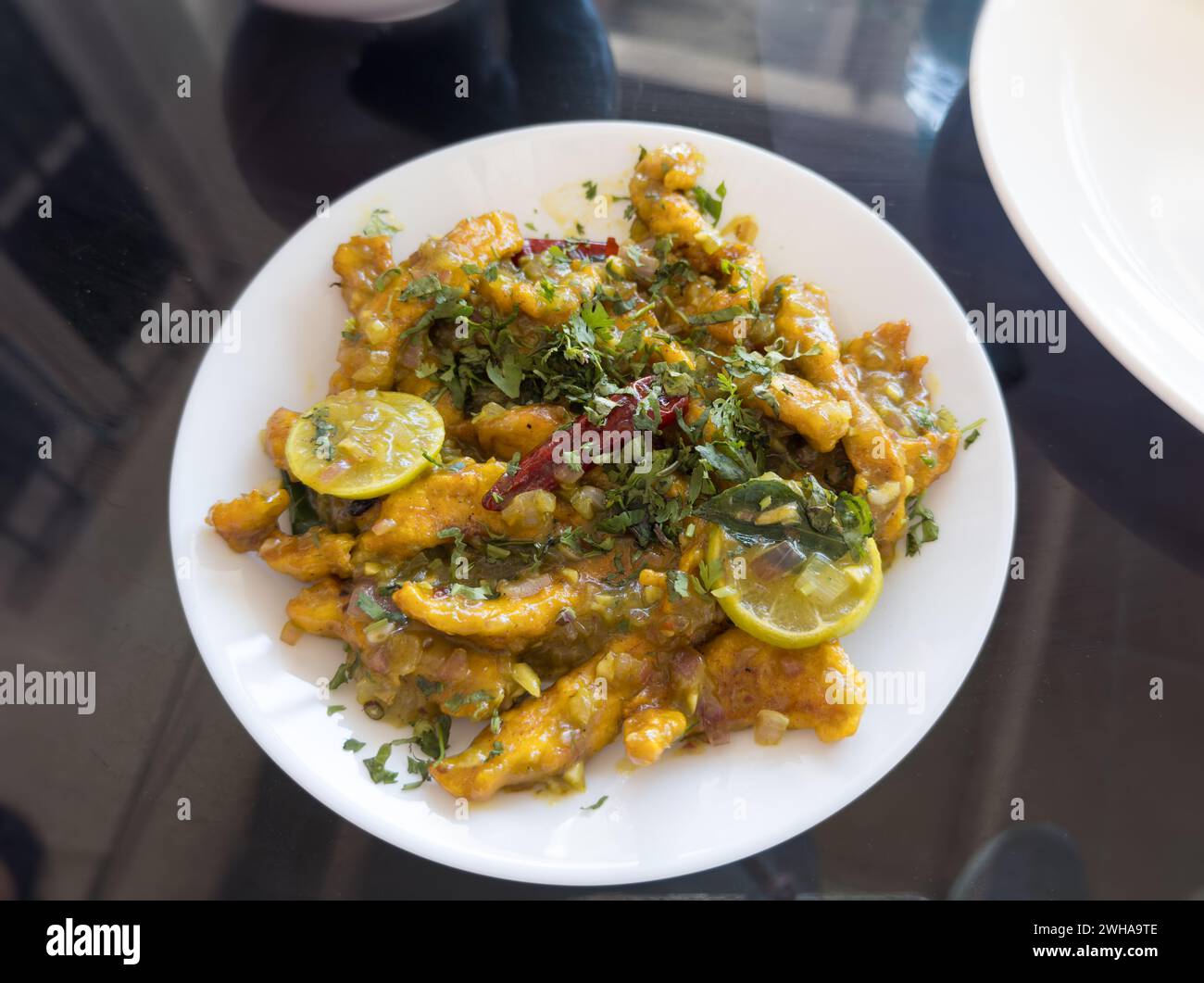 Poulet au citron cuit à la perfection et servi dans une assiette blanche et placé sur fond de table en verre. Banque D'Images