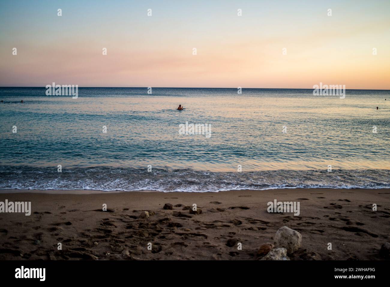 Une scène tranquille comme les gens profitent d'un coucher de soleil nager dans la mer calme, baigné dans les teintes chaudes du crépuscule, créant une atmosphère côtière sereine. Banque D'Images