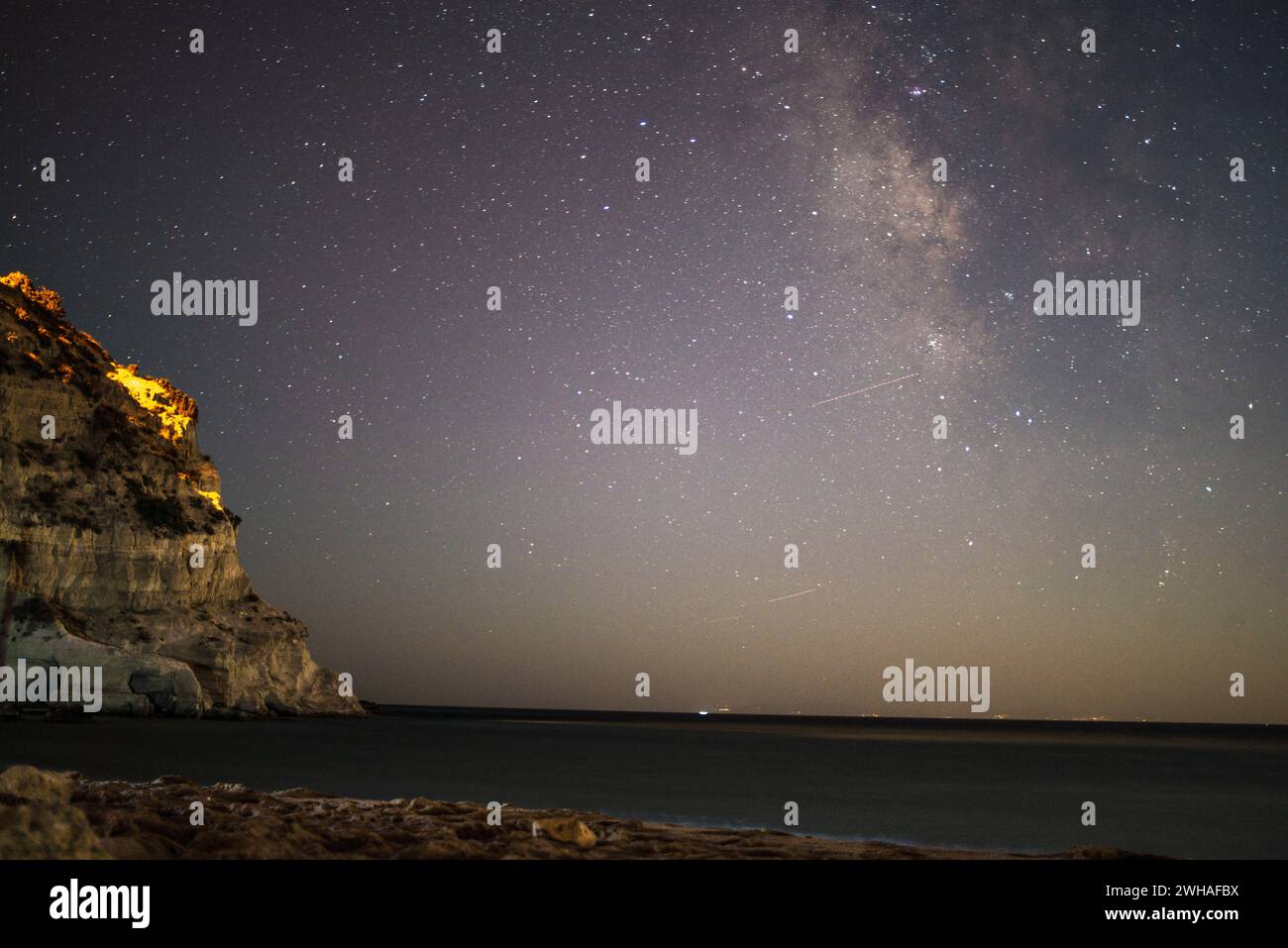 Une scène côtière à couper le souffle où la voie Lactée orne le ciel nocturne sur la mer et la montagne, créant une merveille sereine et cosmique. Banque D'Images