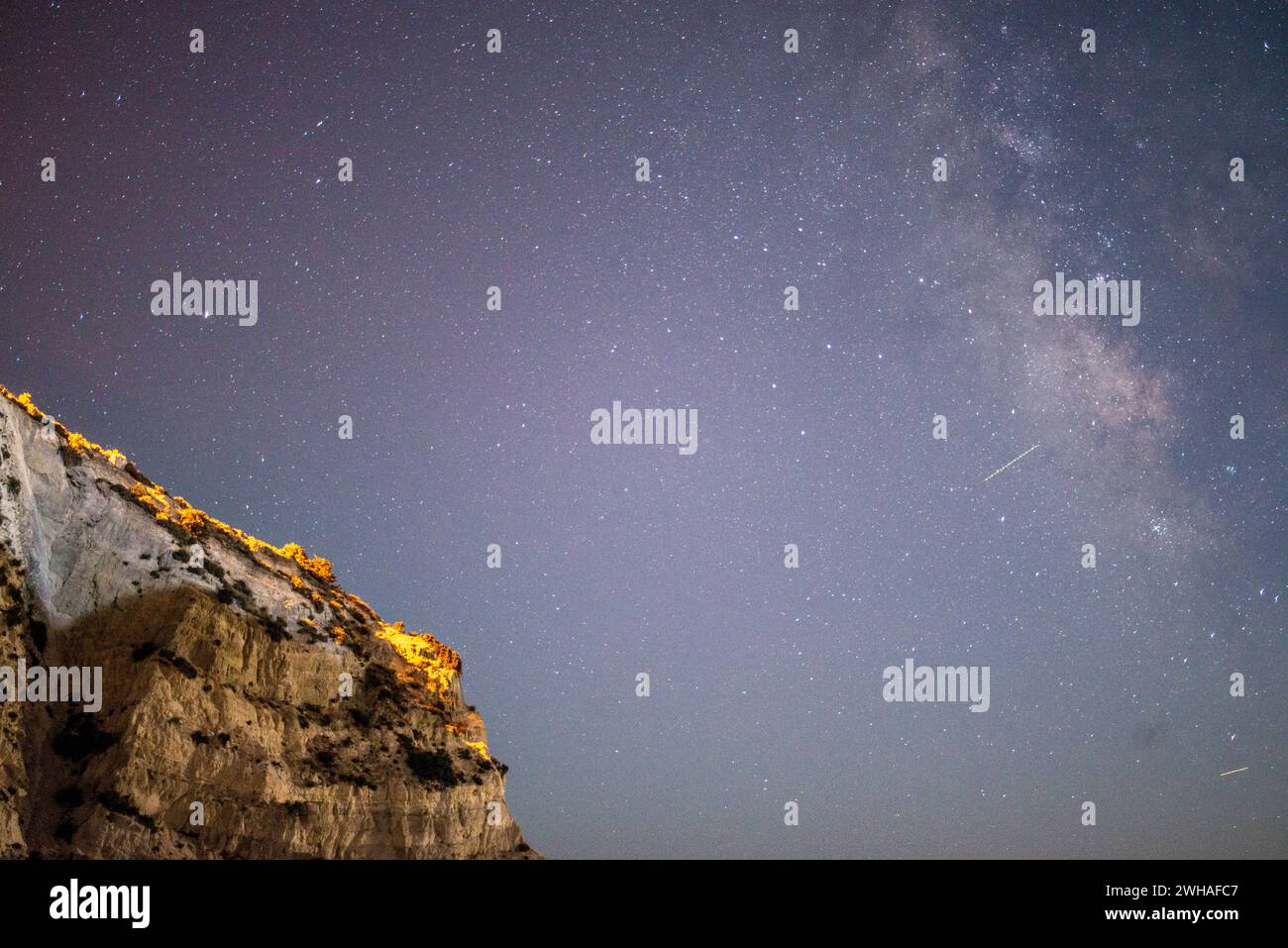 Une scène côtière à couper le souffle où la voie Lactée orne le ciel nocturne sur la mer et la montagne, créant une merveille sereine et cosmique. Banque D'Images Une scène côtière à couper le souffle où la voie Lactée orne le ciel nocturne sur la mer et la montagne, créant une merveille sereine et cosmique. Banque D'Images