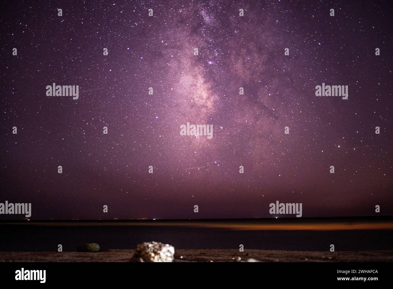 Une scène côtière à couper le souffle où la voie Lactée orne le ciel nocturne sur la mer et la montagne, créant une merveille sereine et cosmique. Banque D'Images