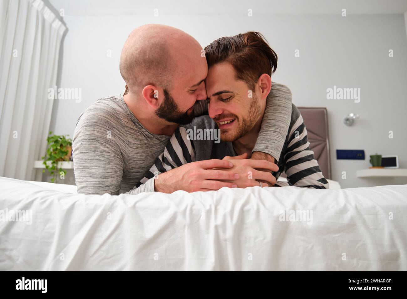 Couple heureux homosexuel embrassant dans l'amour dans le lit ensemble. Banque D'Images