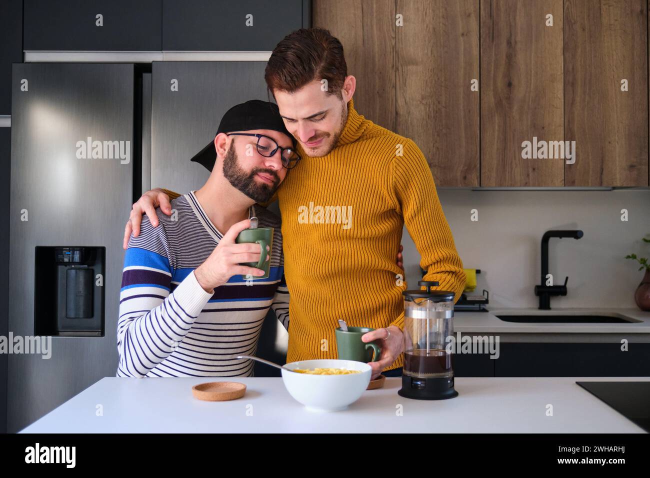 Couple homosexuel embrassant et prenant le petit déjeuner à la cuisine. Banque D'Images