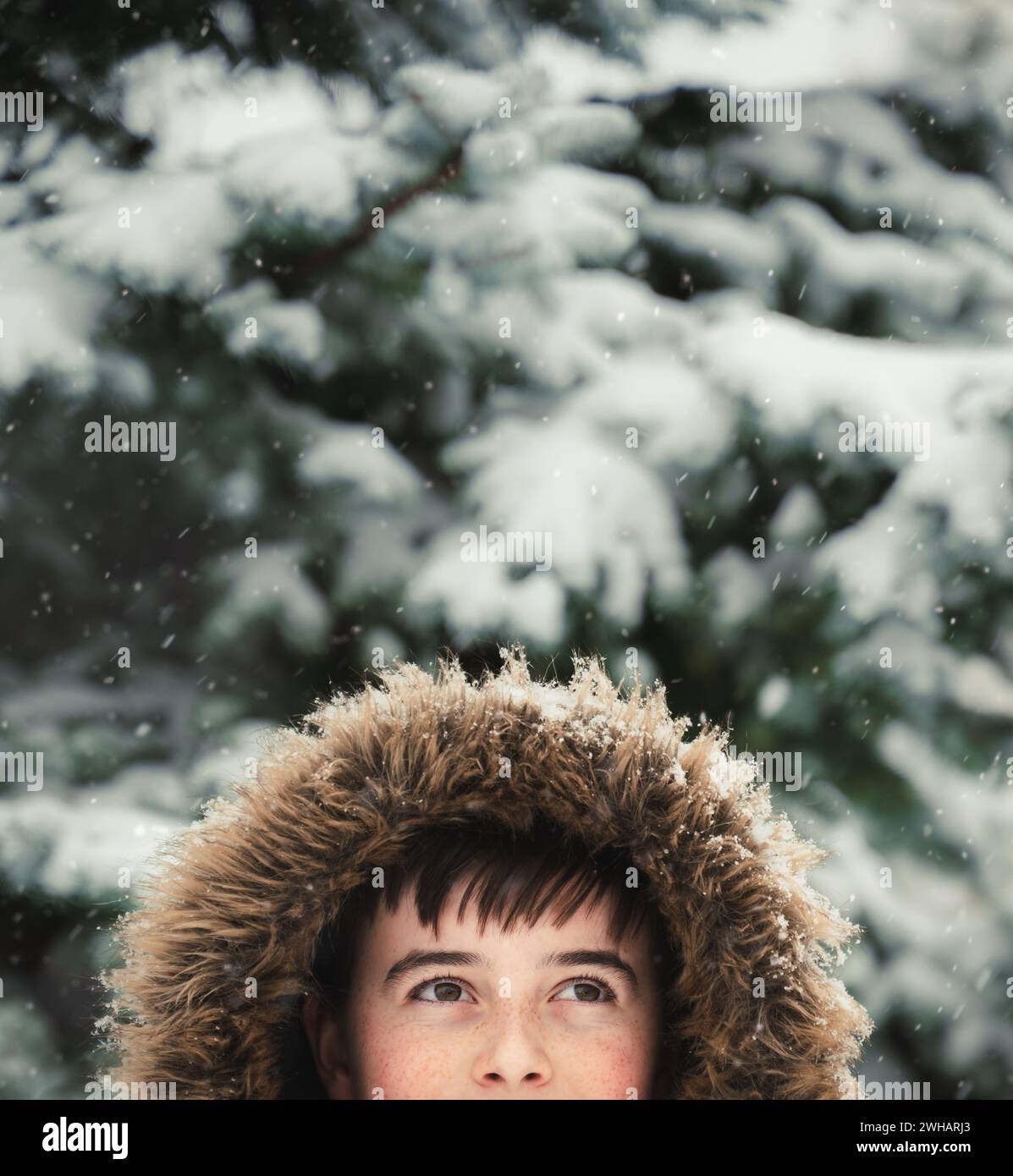 Heureux garçon portant manteau avec capuche fourrure dehors dans la neige le jour d'hiver. Banque D'Images