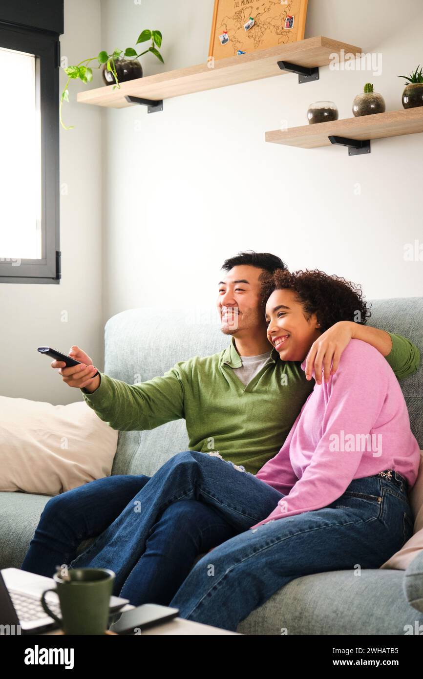 Couple multiracial sourire et regarder la télévision, le film ou le film ensemble sur le canapé. Banque D'Images