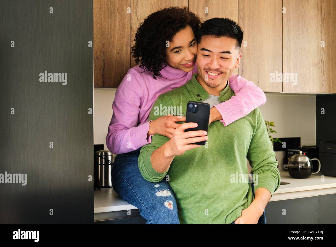 Couple heureux multiethnique utilisant le smartphone ensemble dans la cuisine. Banque D'Images