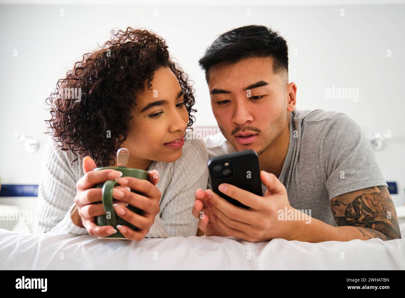 Couple multiethnique utilisant le smartphone sur le lit. Banque D'Images