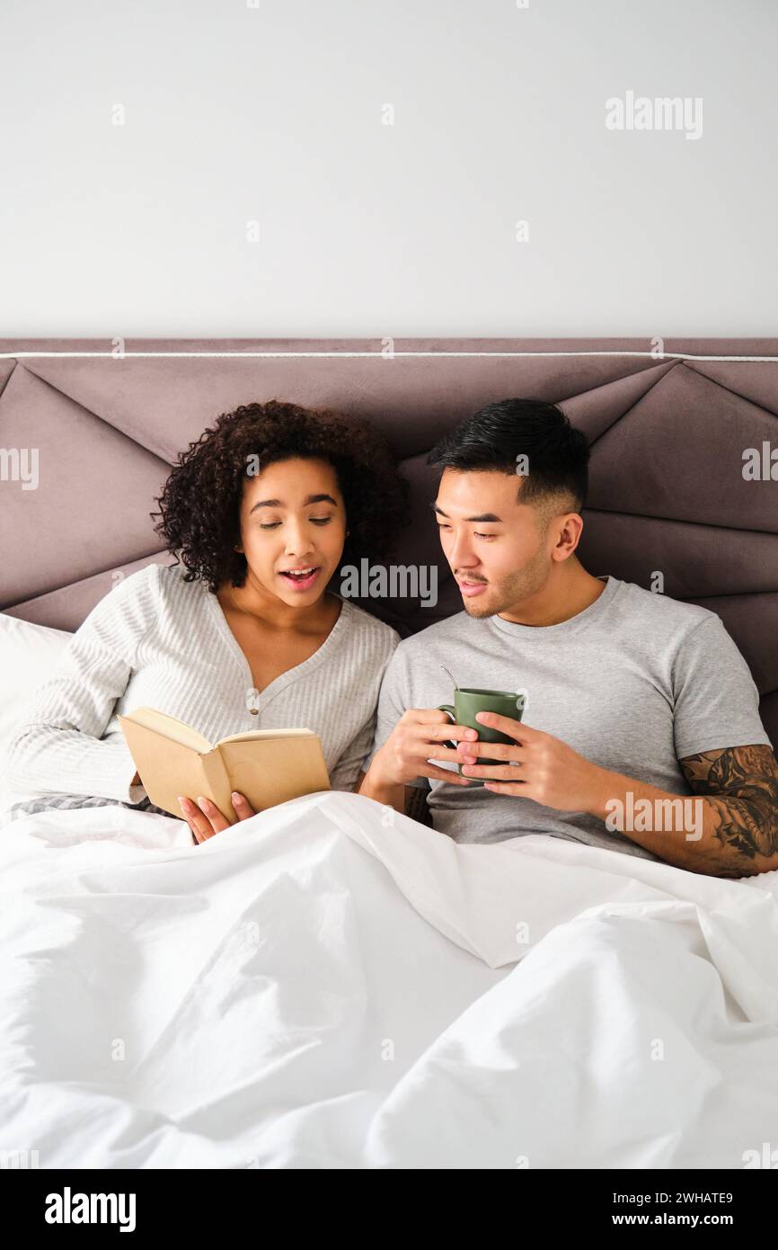 Couple multiracial apprenant les langues avec un livre sur le lit ensemble. Banque D'Images