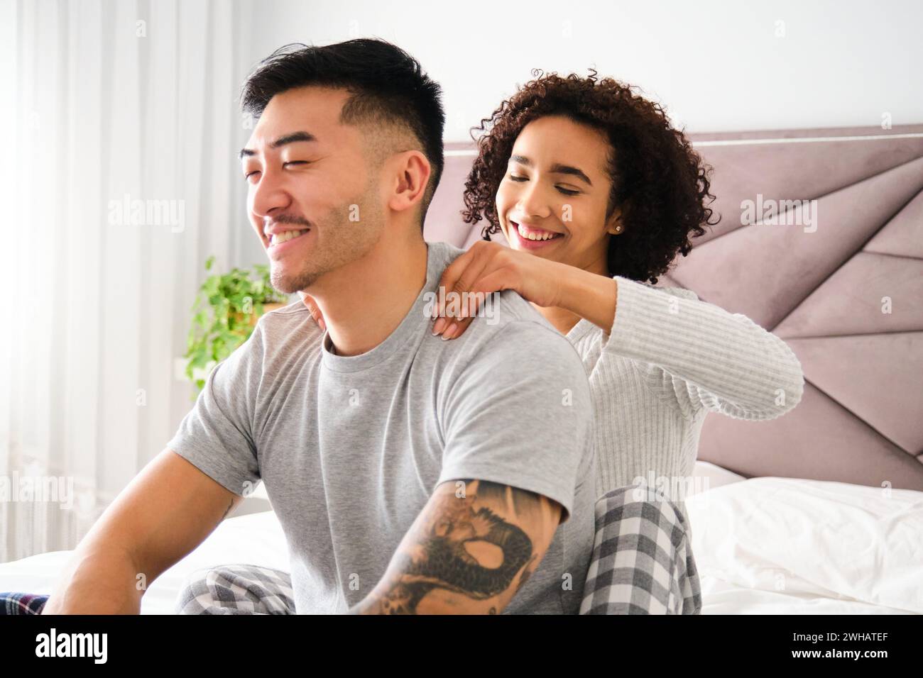Femme latine massant les épaules de son petit ami asiatique sur le lit. Banque D'Images