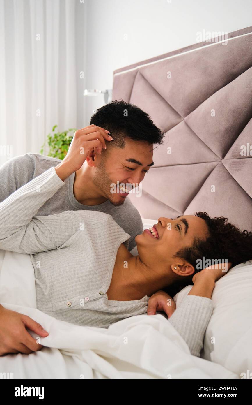 Couple romantique diversifié se réveillent ensemble dans le lit pendant la lune de miel. Banque D'Images