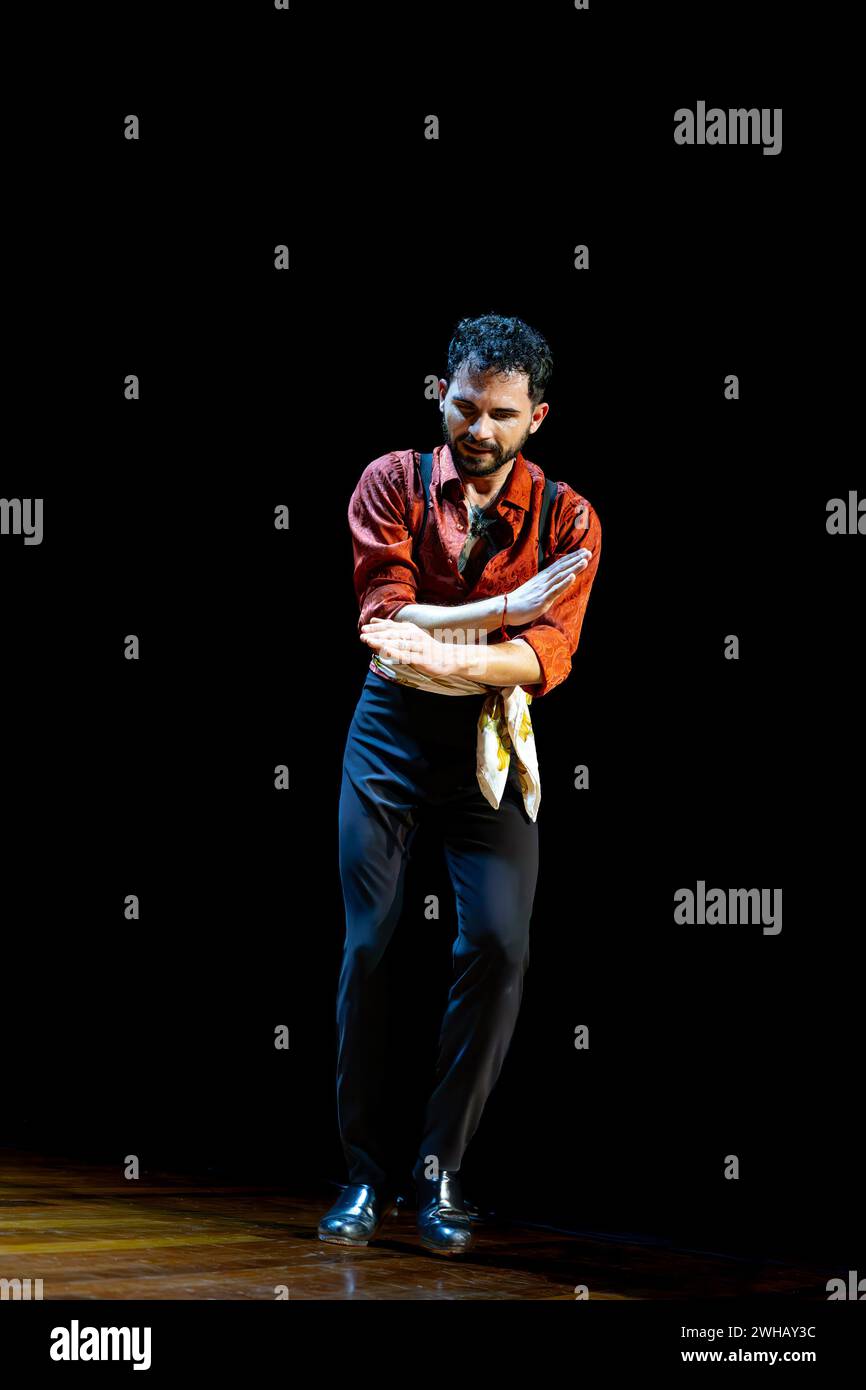 Danseur de flamenco masculin exprime une profonde émotion à travers sa pose sur une scène sombre, portant une chemise rouge vif, photo verticale. Banque D'Images