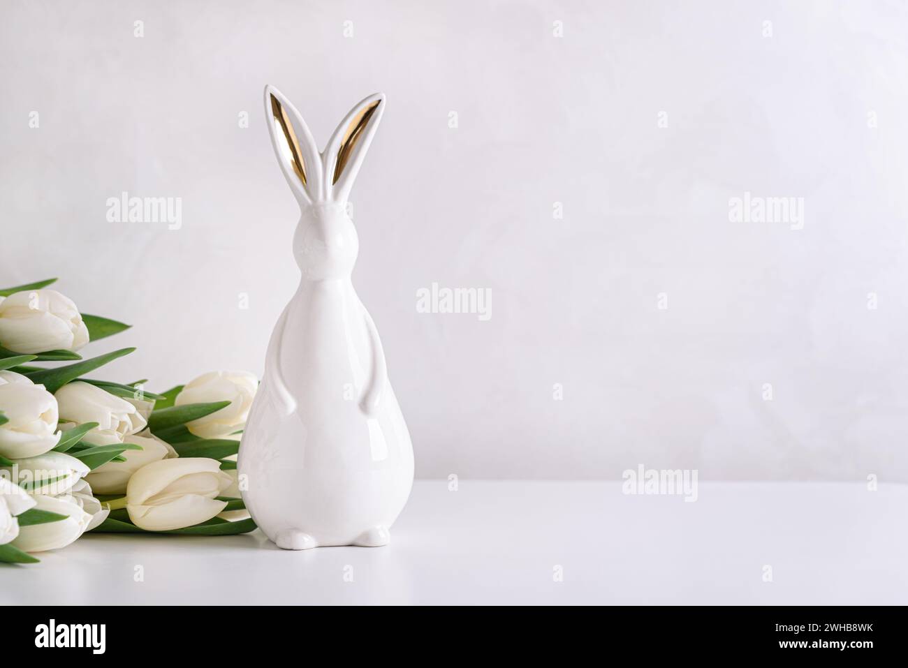 Figurine de lapin de Pâques avec bouquet de tulipes blanches sur fond blanc. Concept de célébration de Pâques. Espace de copie. Vue avant Banque D'Images