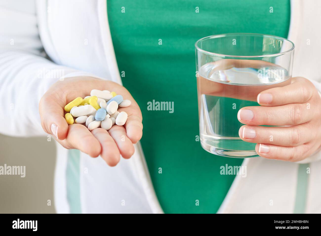 Plan d'une main de jeune femme méconnaissable montrant de nombreuses pilules et un verre d'eau Banque D'Images