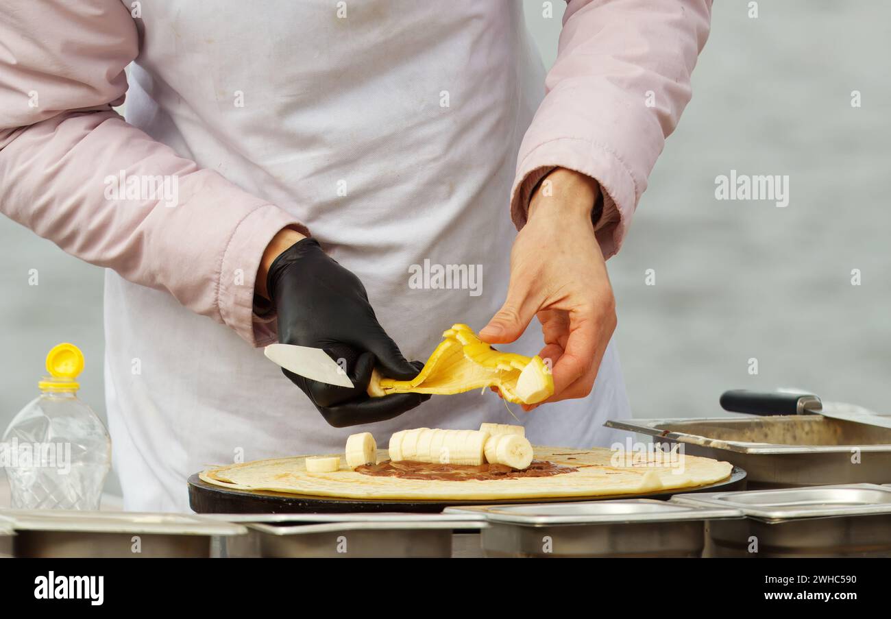 Corps de milieu de section d'un homme fabriquant des crêpes sucrées avec de la banane et du chocolat au marché alimentaire de rue au front de mer de Naplavka à Prague, République tchèque Banque D'Images