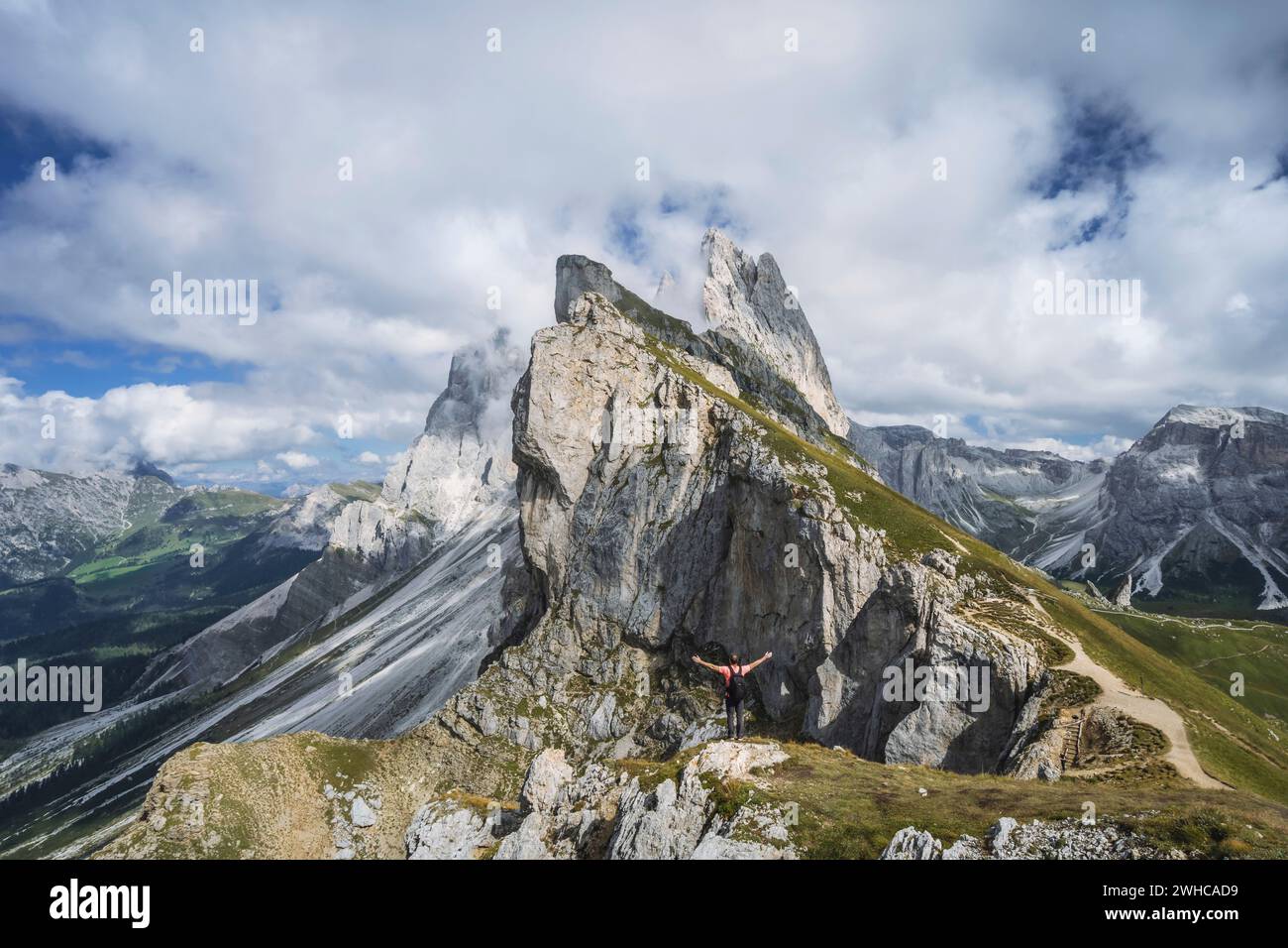Un homme levant les mains devant les sommets épiques de Furchetta et Sass Rigais à Seceda, dans les Alpes Dolomites, dans la chaîne de montagnes Odle, Tyrol du Sud, Italie, Europe. Concept de vacances de voyage. Banque D'Images