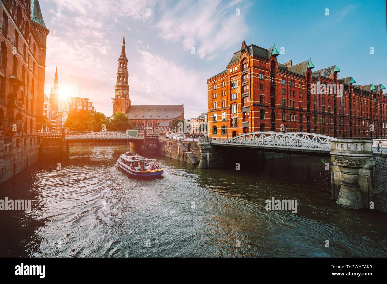 Bateau de croisière touristique sur un canal avec des ponts dans l'ancien quartier d'entrepôts Speicherstadt à Hambourg en heure d'or coucher de la lumière, de l'Allemagne. Banque D'Images