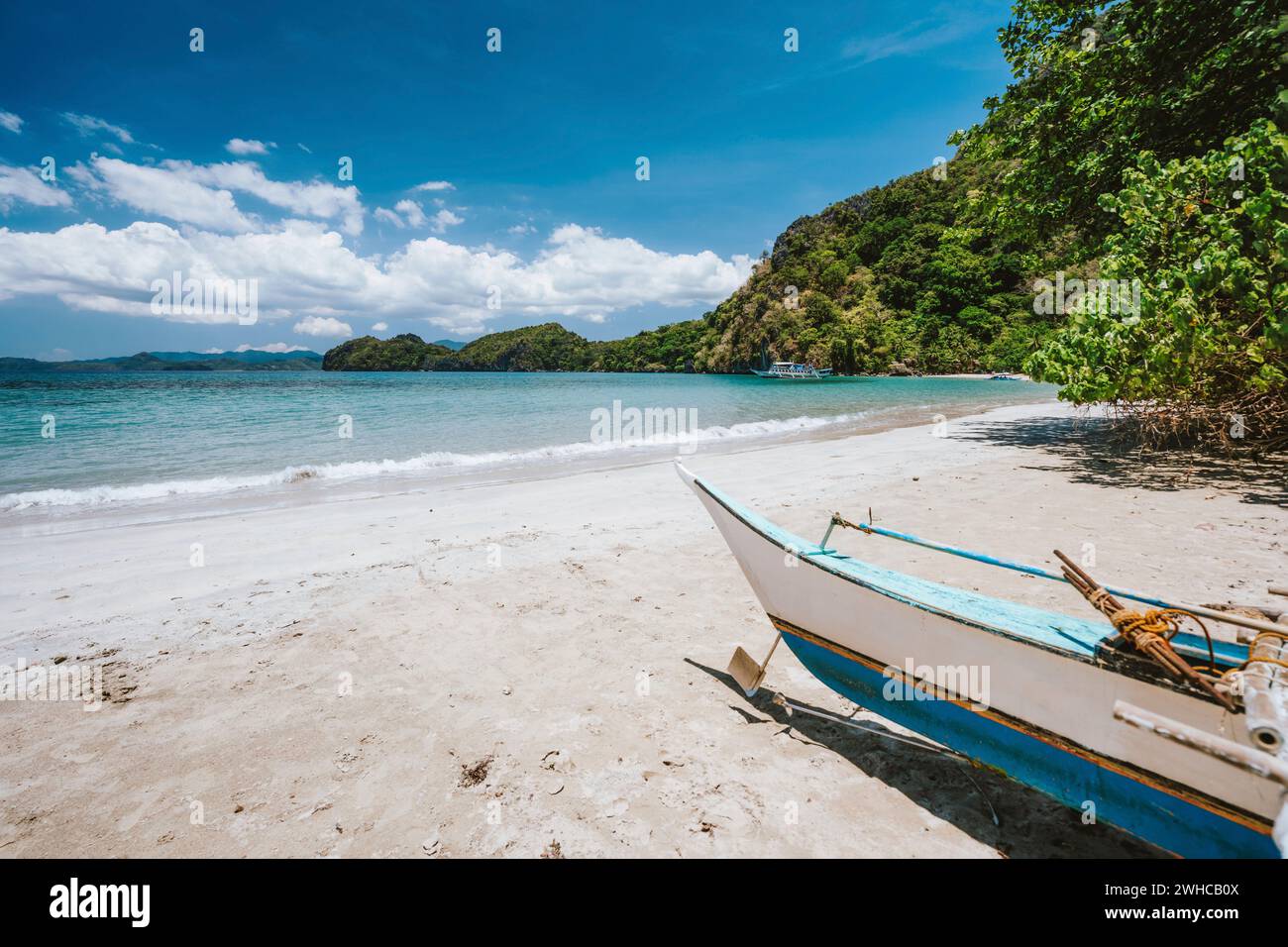 Bateau traditionnel banca en face de la plage tropicale avec lagon bleu exotique. El Nido, Philippines. Banque D'Images