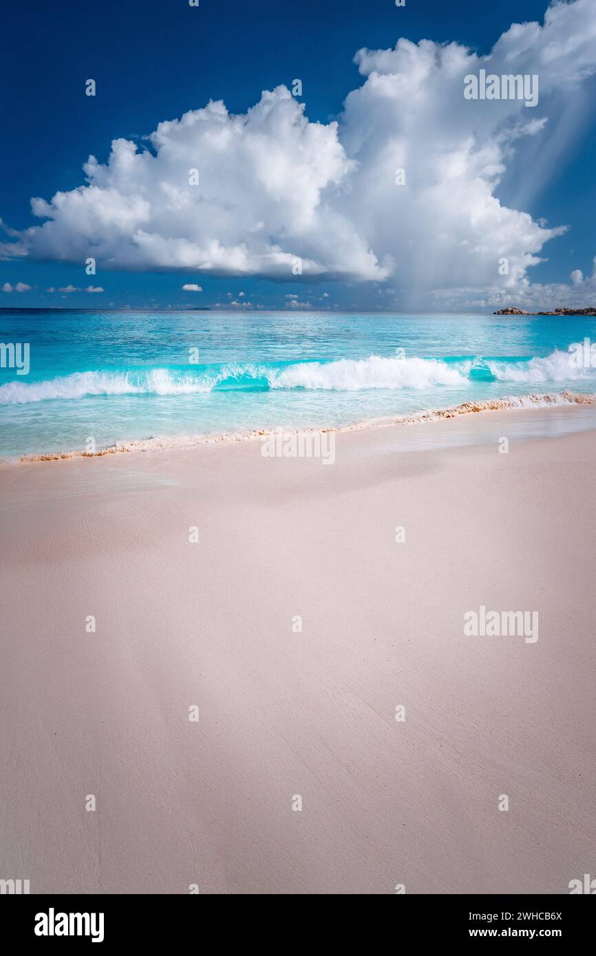 Belle vague de ocen blanc qui se déforme vers la plage de sable tropical. Nuages moelleux au-dessus de la mer bleue. Grande Anse, Seychelles. Banque D'Images
