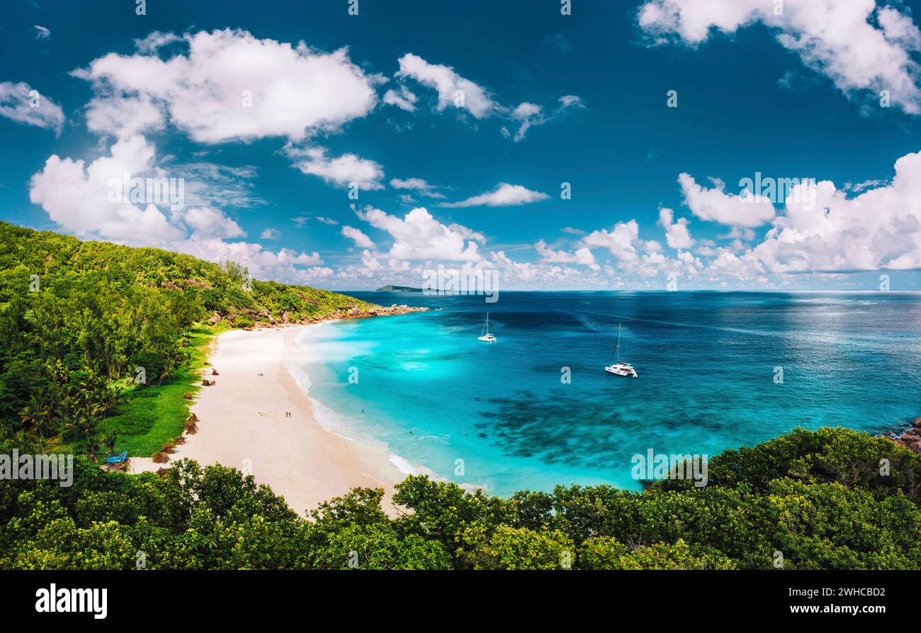 Plage de Grand Anse sur l'île de la Digue aux Seychelles vue panoramique aérienne. Plage de sable blanc avec lagon bleu océan et yacht catamaran amarré. Banque D'Images