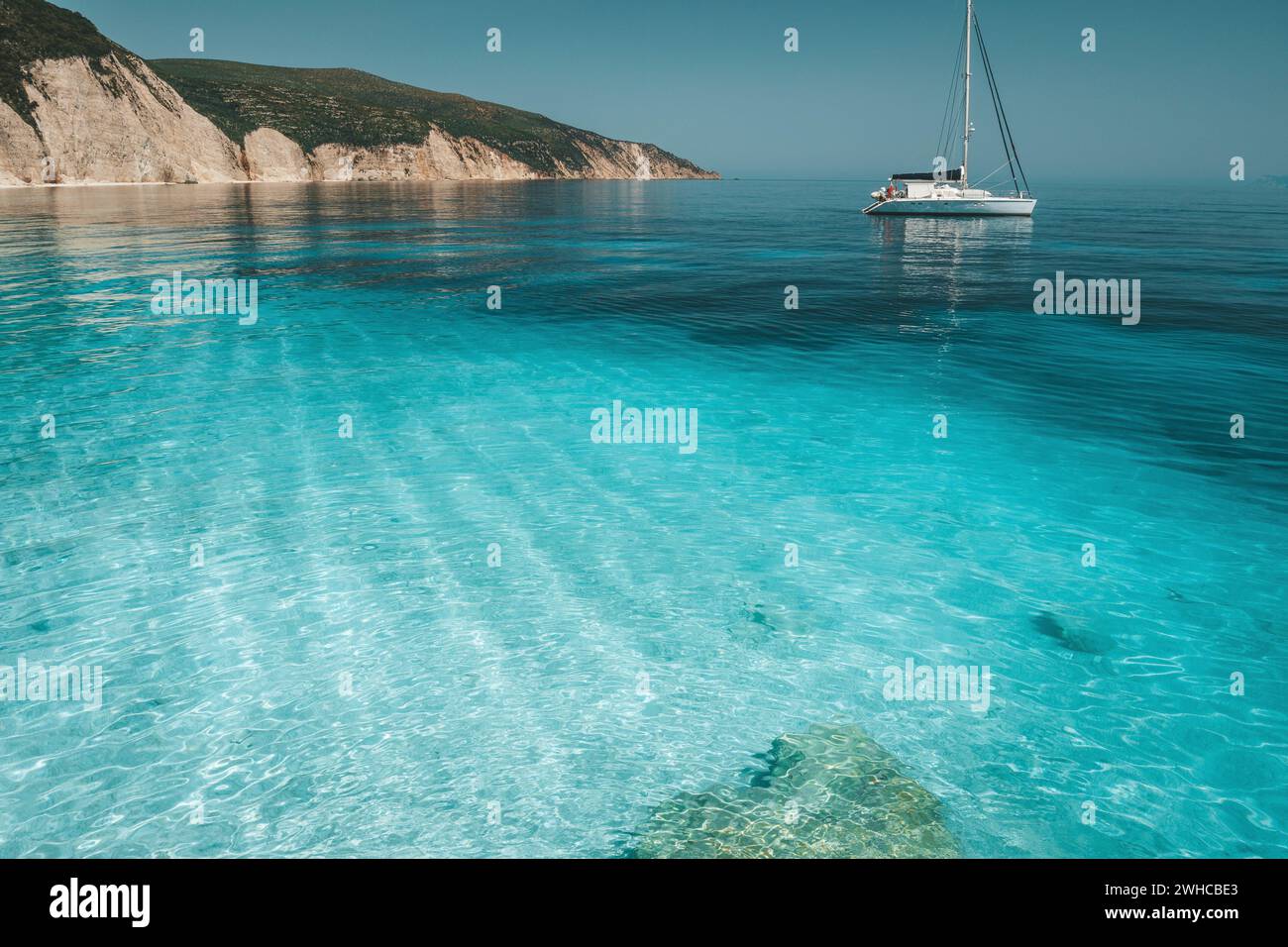 Lagon bleu azur avec des vagues calmes et d'un catamaran à voile à la voile. Littoral falaise rocheuse en arrière-plan. Banque D'Images