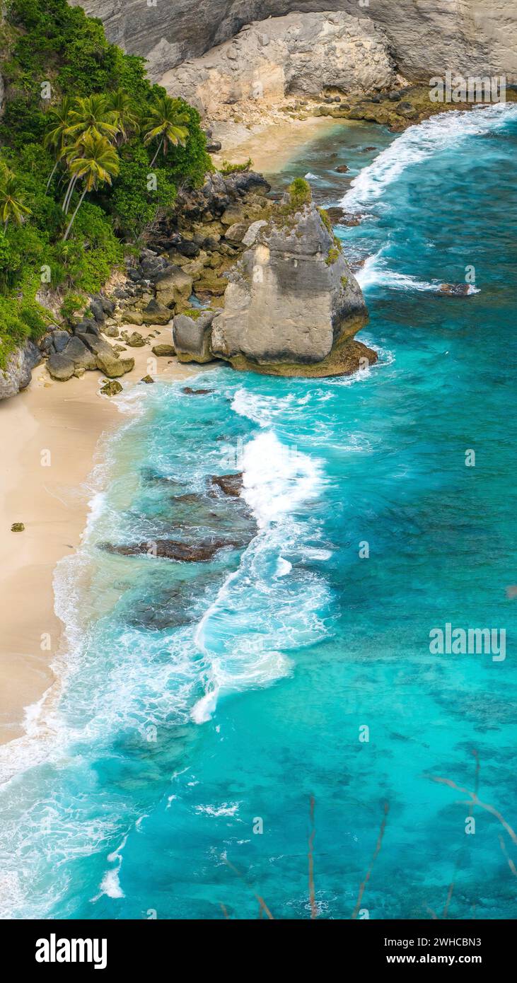 Rock dans l'océan avec de beaux palmiers derrière la plage d'Atuh sur l'île Nusa Penida, Indonésie. Banque D'Images