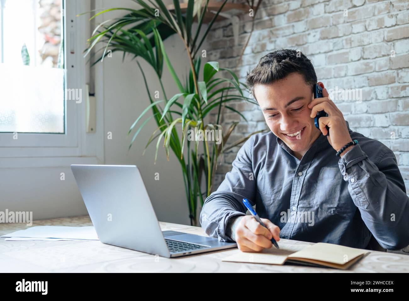 Homme d'affaires souriant portant des lunettes parlant au téléphone, assis au bureau avec un ordinateur portable, sympathique Manager consultant le client par téléphone, heureux homme discutant avec des amis distraits du travail Banque D'Images