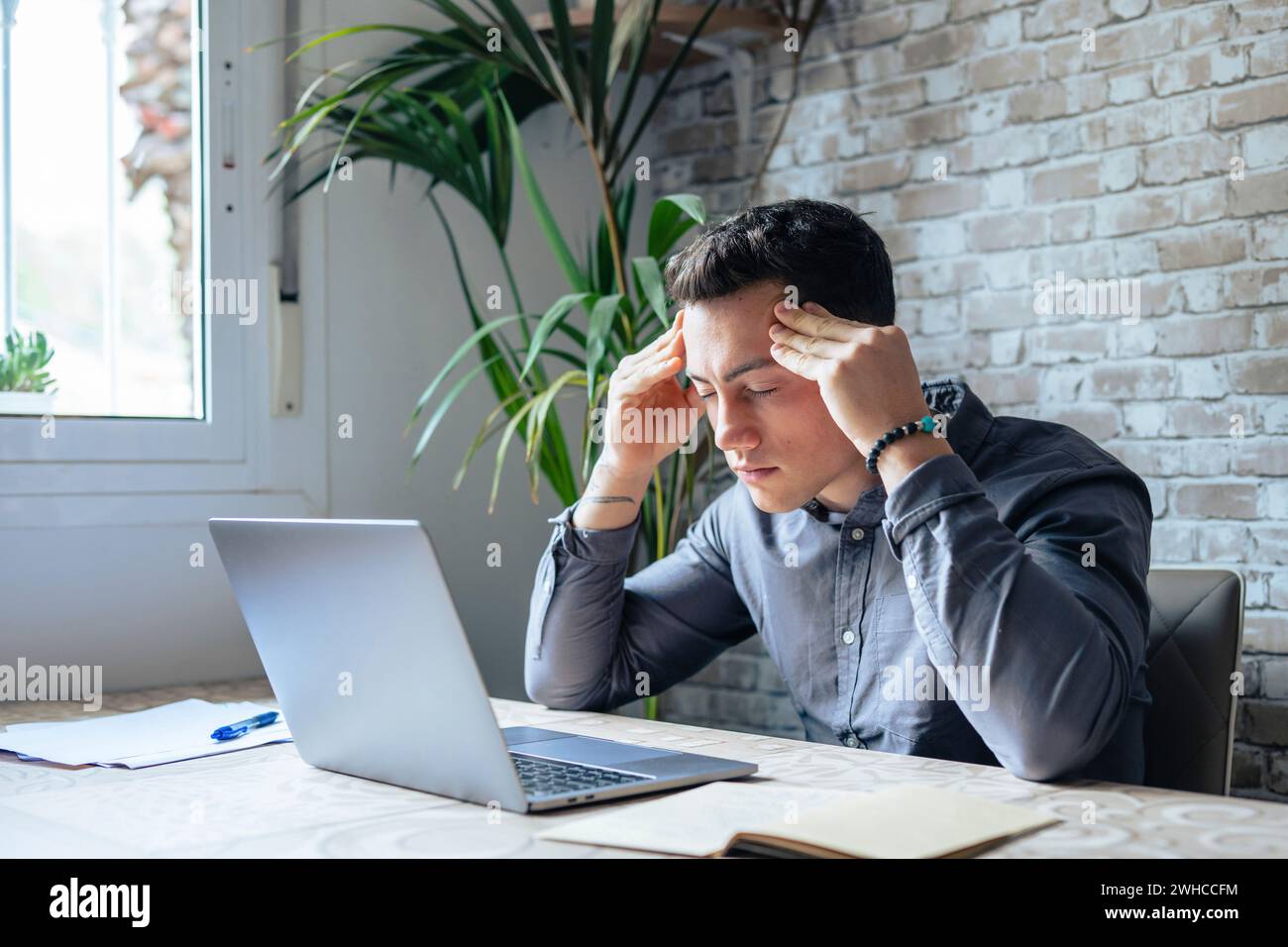 Homme fatigué stressé dans la douleur ayant une forte attaque terrible de mal de tête après le travail d'ordinateur portable, fatigué gars épuisé souffrant de migraine chronique massant tempes pour soulager la tension de mal de tête Banque D'Images