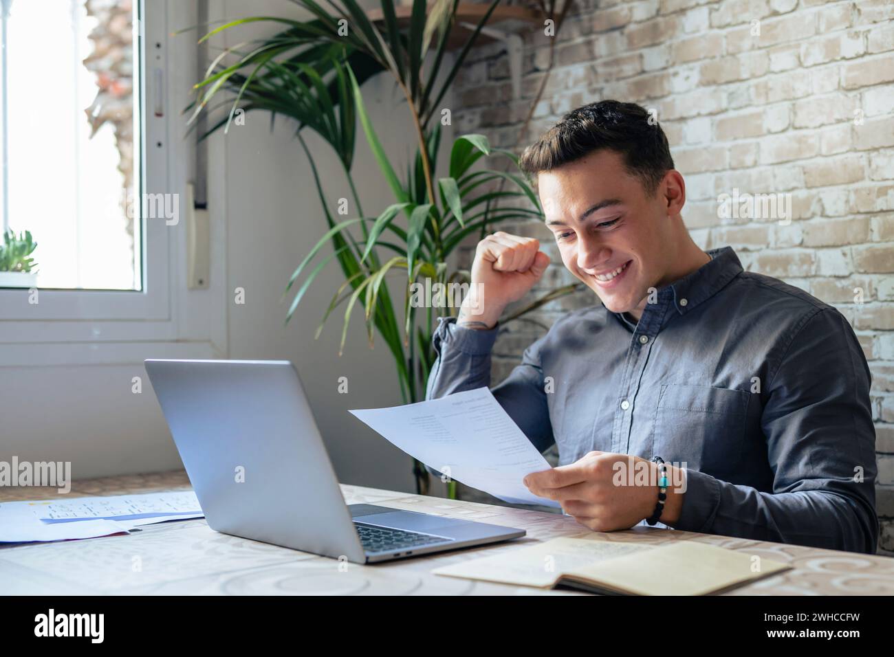 Étudiant homme d'affaires excité lisant la lettre postale ravi par les bonnes nouvelles, heureux gagnant masculin tenant la facture papier avec approbation de prêt célébrer le remboursement des impôts recevoir le paiement de l'augmentation de salaire assis à la table Banque D'Images