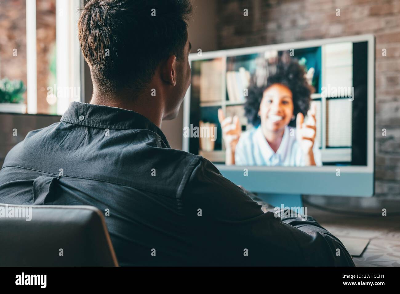 Voir sur l'épaule employeur écouter le candidat à l'entretien d'embauche en ligne utiliser la caméra et le pc. Jeune homme caucasien avec des tatouages à la maison travaillant et parlant en ligne avec une collègue africaine en vidéoconférence. Banque D'Images
