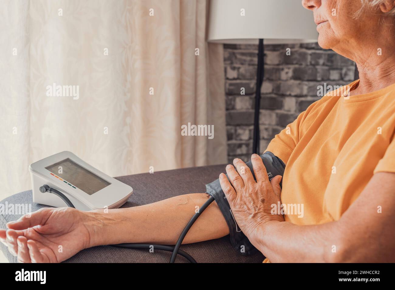La femme aînée principale mesure l'essai d'hypertension basse pression artérielle tenant à l'aide d'un compteur électronique numérique médical assis sur le canapé à la maison, athérosclérose de maladie cardiaque Banque D'Images