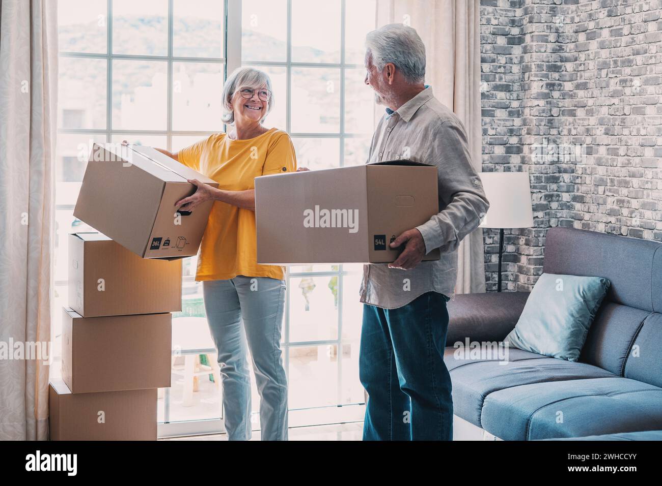 Couple mûr déménageant dans un nouvel appartement, transportant des boîtes en carton dans une pièce vide avec des plantes en pot. Achat de biens immobiliers, relocalisation, nouveau concept de maison. Vue arrière Banque D'Images