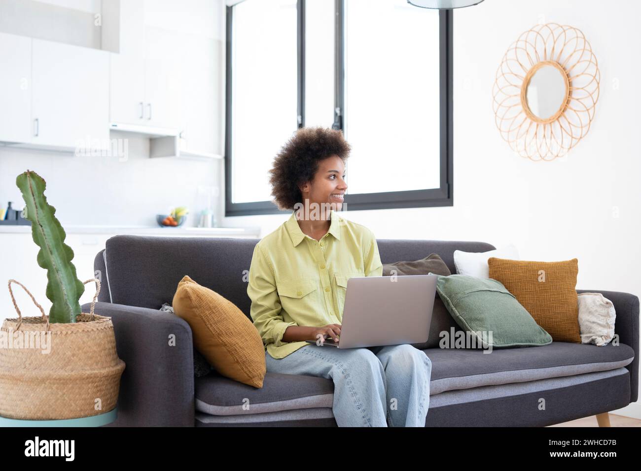 Souriant jeune femme noire à l'aide d'un ordinateur portable, reposant sur un canapé confortable, parler sur un appel vidéo, discuter en ligne, naviguer sur Internet, regarder un film, faire des achats sur Internet. Utilisateur de gadget numérique paresseux Banque D'Images