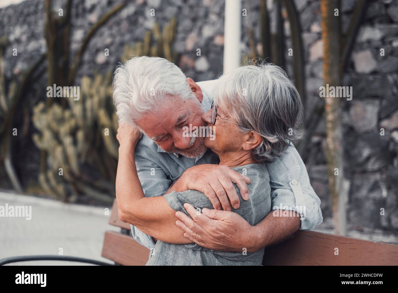 Femme d'âge mûr assise sur le banc du parc avec un vieil homme l'embrassant par le dos. Couple de personnes retraitées se relaxant et profitant du coucher de soleil ensemble outdo Banque D'Images
